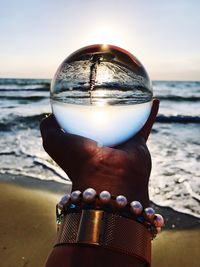 Close-up of hand holding crystal ball against sea