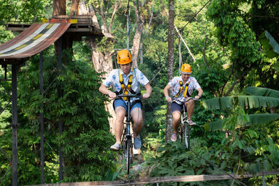 Siblings driving bicycles on ropes against trees in forest