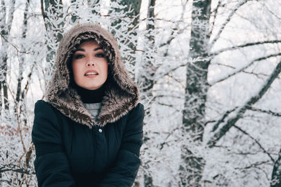 Portrait of woman wearing fur coat standing against trees during winter