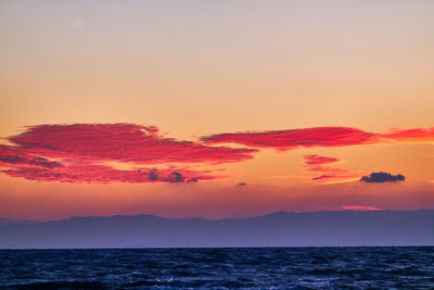 Scenic view of sea and mountains against dramatic sky during sunrise