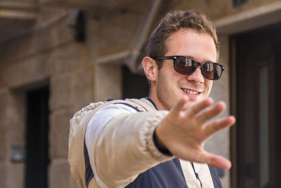 Portrait of smiling young man gesturing while standing outdoors
