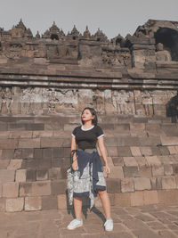 Full length of young woman standing against brick wall