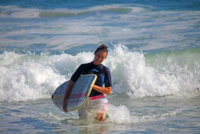 Woman with surfboard walking in sea on sunny day