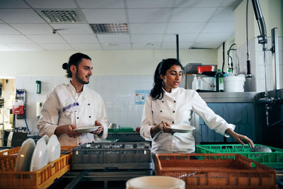 Male and female chefs communicating while holding plates in kitchen