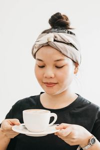 Close-up of smiling young woman holding coffee against white background
