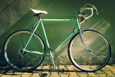 Bicycle parked on footpath against wall during sunny day