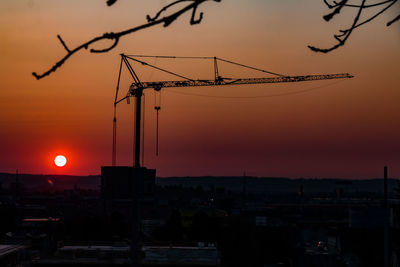 Silhouette cranes at construction site during sunset