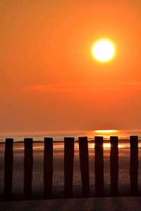 Wooden posts on beach against sky during sunset