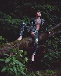 Young man sitting on fallen tree in forest