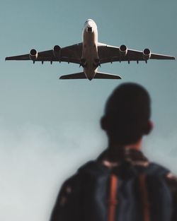 Rear view of person looking at airplane flying in sky