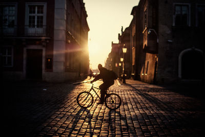 Silhouette man riding bicycle on street during sunrise