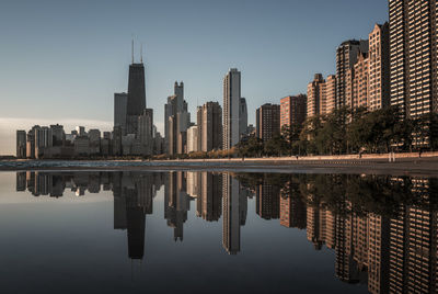 Reflection of buildings in river against clear sky