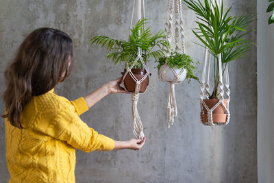 Side view of woman hanging plants at home