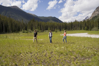 Full length of friends standing on grassy field against mountains