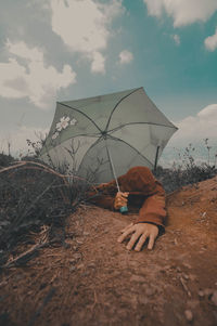 Tired man with umbrella on mountain against sky