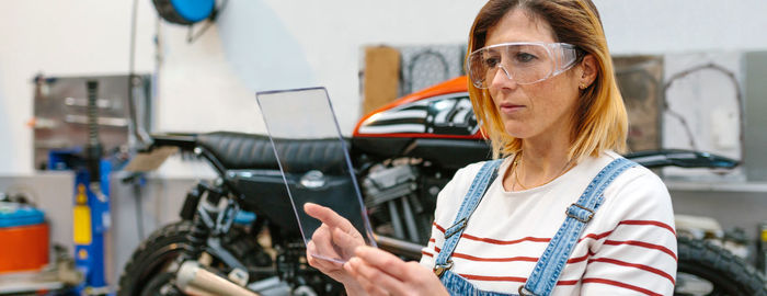 Female mechanic with security glasses holding transparent tablet