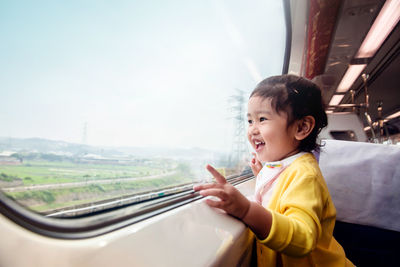 Side view of cute girl looking through window in train