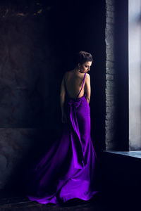 Young woman standing near a window in purple long dress