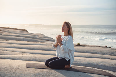 Full length of woman meditating at beach against sea