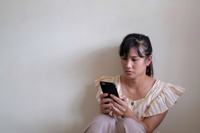 Young woman using mobile phone while sitting on wall