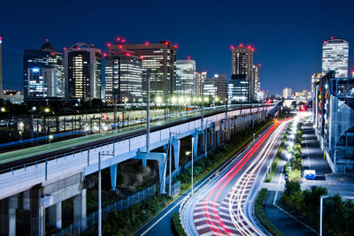 Light trails on road amidst buildings against sky at night