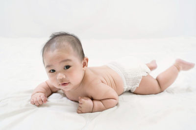 Training tummy time of adorable young asian newborn little baby boy prone on the bed.