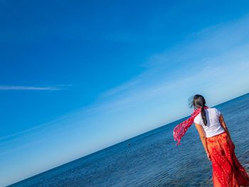 Woman standing by sea against blue sky