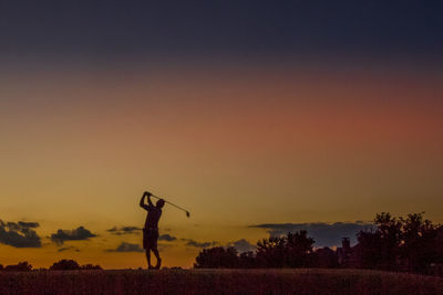 Man holding stick on field against sky during sunset