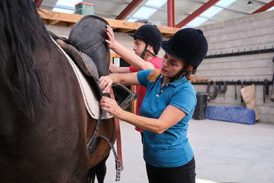 Mother and son putting the saddle on a horse before riding.