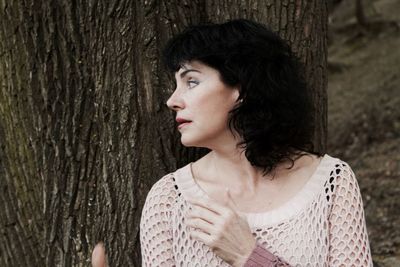 Side view of woman against tree trunk while looking away