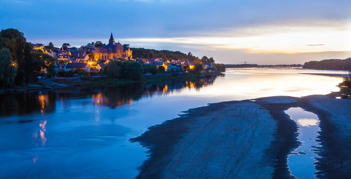 Scenic view of lake by illuminated buildings against sky at sunset