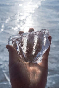 Close-up of hand holding ice over sea