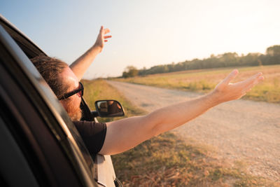 Man picking from car window against sky