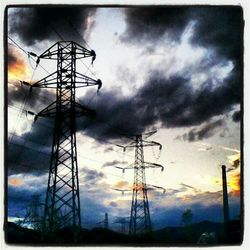 Low angle view of electricity pylon against cloudy sky