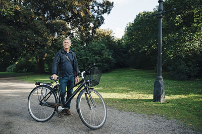 Portrait of senior man standing with bicycle in park