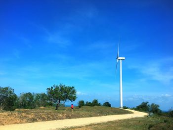Man standing on field by windmill against blue sky