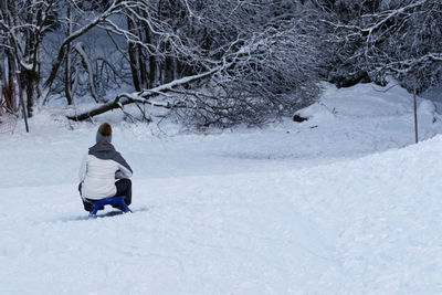 Rear view of woman crouching on snow covered land