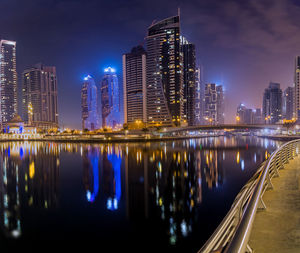 Illuminated buildings by river against sky in city at night