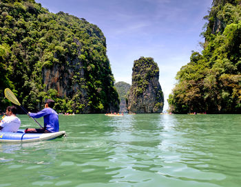 People sitting on rock by lake against sky