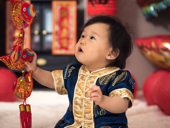 Baby girl in traditional clothing touching decoration at home during chinese new year