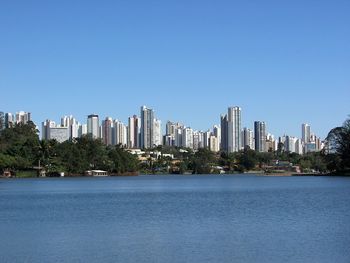 Sea with modern buildings in background against clear blue sky