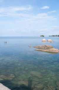 People in water by rocks against cloudy sky