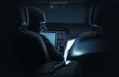 Rear view of computer hacker with laptop sitting in car