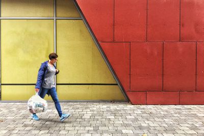 Side view of woman with polyethene bag walking on footpath