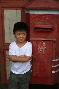 Smiling boy with arms crossed while standing against door