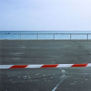 Abstract shot of red-white do-not-enter tape on asphalt road against sea horizon.