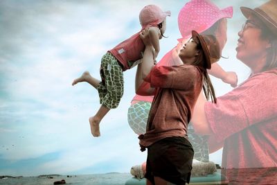 Multiple image of playful mother carrying daughter at beach against sky