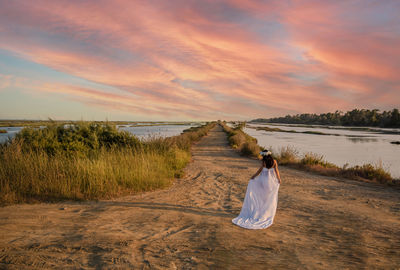 Rear view of woman on beach against sky during sunset