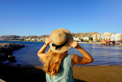 Sunset back view of girl holding straw hat in crotone city on calabria coast, italy