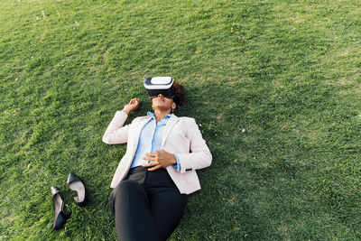 Businesswoman wearing virtual reality simulator lying on grass